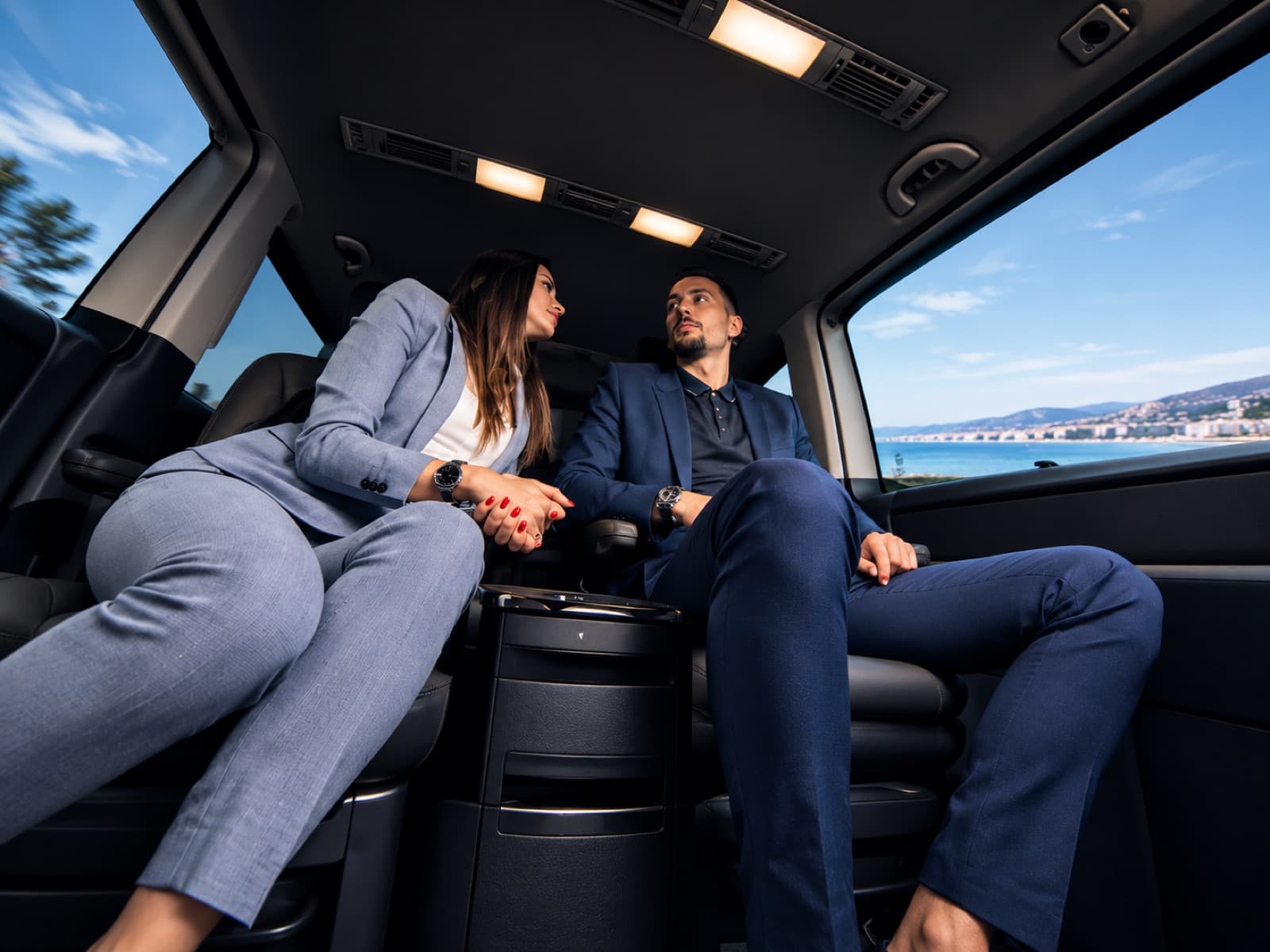 A well-dressed couple relaxing in the cabin of a premium Mercedes van with a coastal view